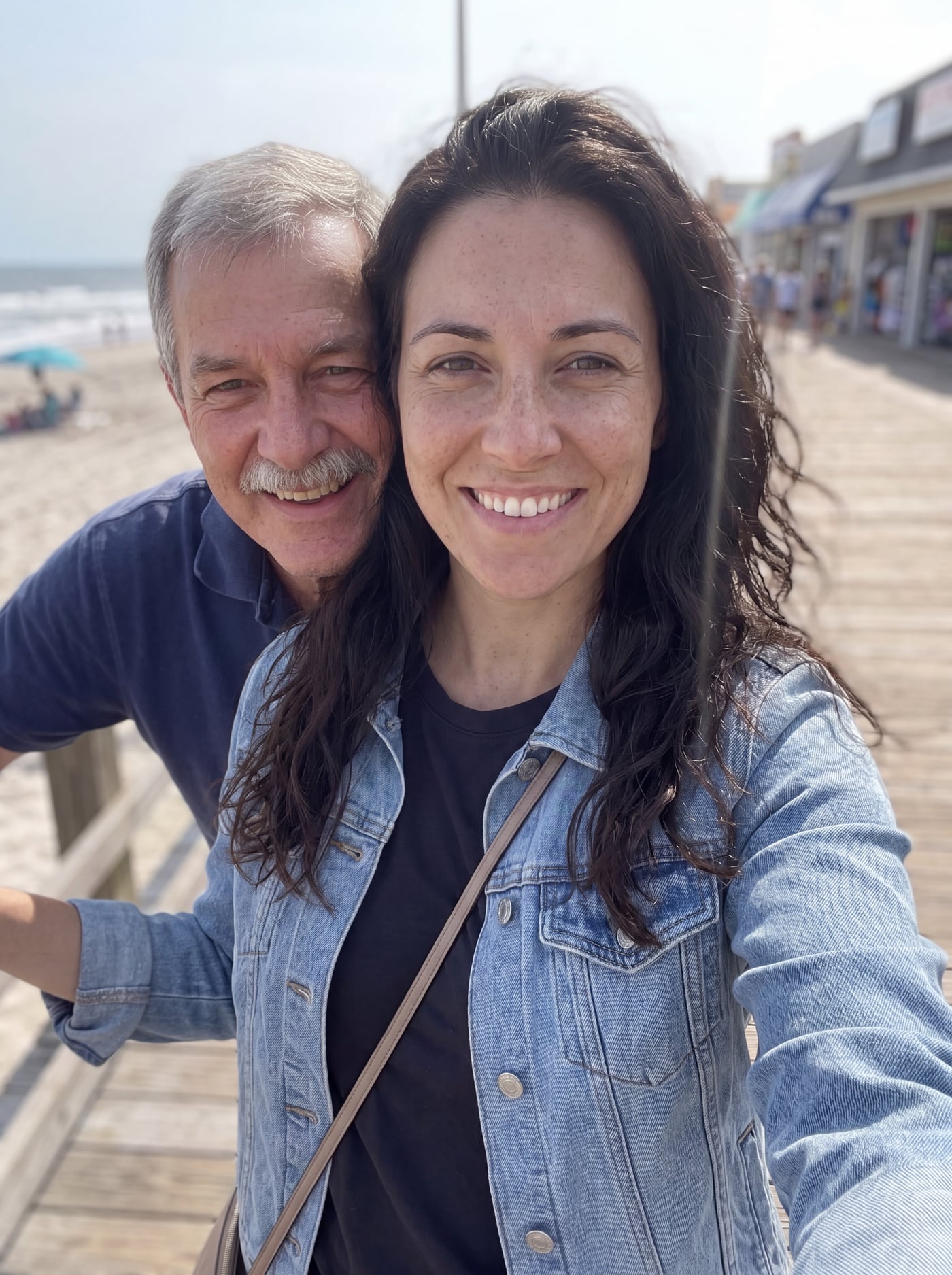 A woman on a beach boardwalk with her father leaning in beside her
